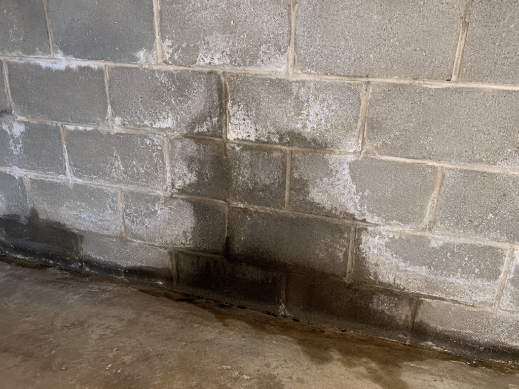 Water stain and efflorescence on a concrete block basement wall before waterproofing.