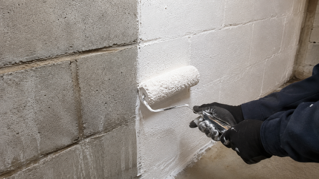 Applying cementitious waterproofer to bare basement block walls from the inside.